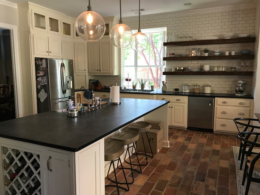 Large country l-shaped eat-in kitchen in Dallas with a farmhouse sink, white cabinets, white splashback, subway tile splashback, stainless steel appliances, with island, raised-panel cabinets, brick floors and multi-coloured floor.