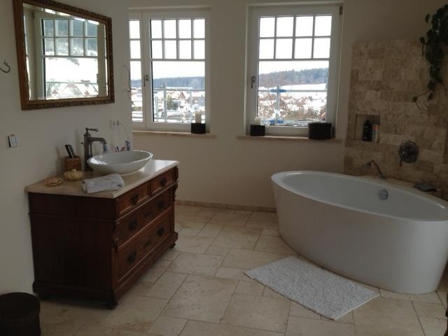 This is an example of an expansive country master bathroom in Hamburg with flat-panel cabinets, brown cabinets, a curbless shower, a one-piece toilet, beige tile, stone slab, beige walls, limestone floors, a vessel sink, wood benchtops, beige floor and an open shower.