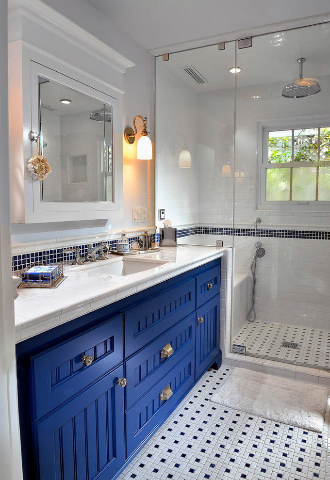 Photo of a beach style 3/4 bathroom in Orange County with white walls, mosaic tile floors, recessed-panel cabinets, blue cabinets, an alcove shower, black and white tile, ceramic tile, an undermount sink, tile benchtops, multi-coloured floor and a hinged shower door.