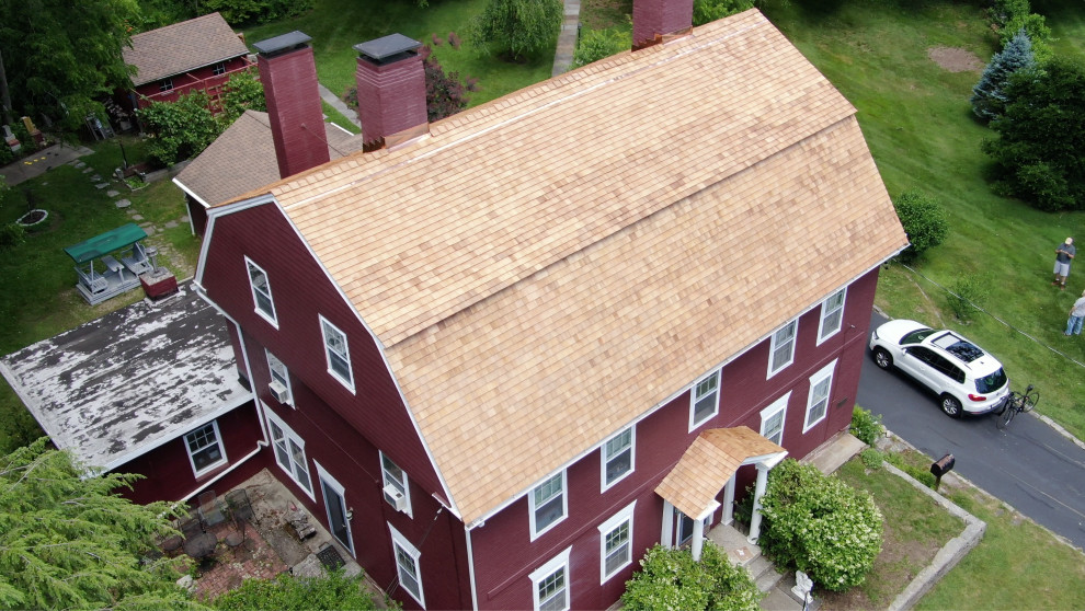 Photo of a large traditional three-storey red house exterior in Bridgeport with painted brick siding, a gambrel roof, a shingle roof and a brown roof.