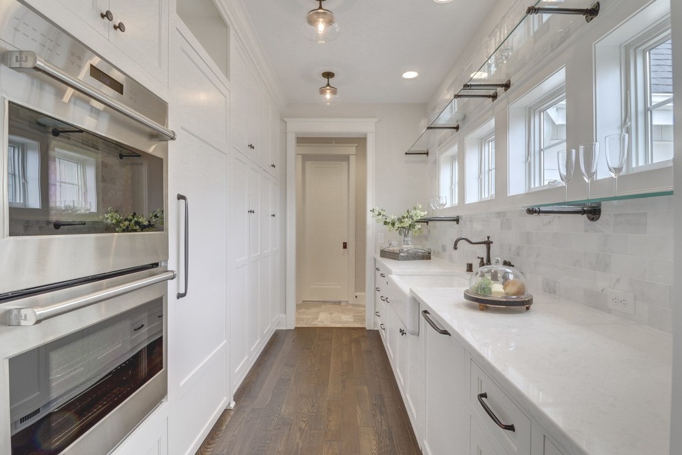 Design ideas for a small traditional galley separate kitchen in Minneapolis with a farmhouse sink, shaker cabinets, white cabinets, granite benchtops, grey splashback, marble splashback, panelled appliances, dark hardwood floors, no island, brown floor and white benchtop.