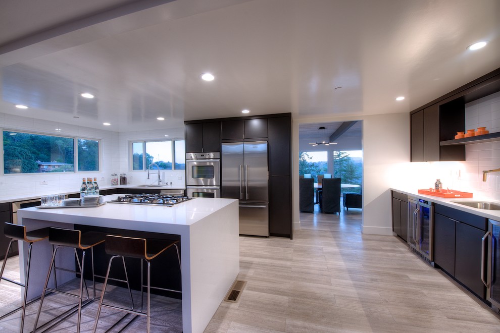 Inspiration for a large midcentury u-shaped eat-in kitchen in San Francisco with an undermount sink, flat-panel cabinets, dark wood cabinets, quartz benchtops, white splashback, subway tile splashback, stainless steel appliances, light hardwood floors and with island.