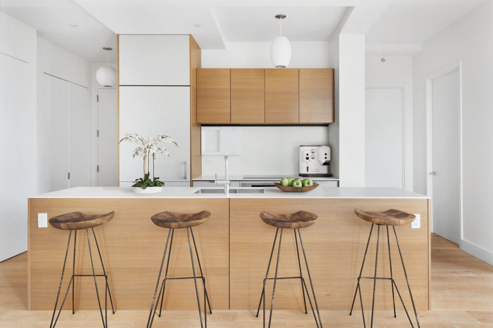 Mid-sized contemporary single-wall eat-in kitchen in New York with a drop-in sink, flat-panel cabinets, beige cabinets, quartz benchtops, white splashback, ceramic splashback, stainless steel appliances, light hardwood floors, with island, beige floor and white benchtop.