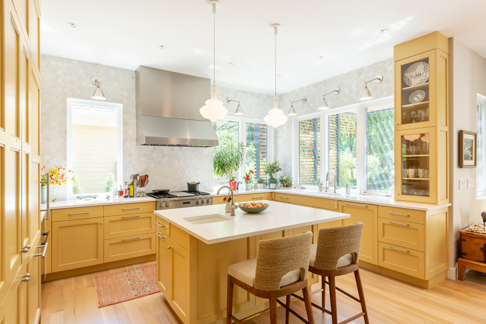 Example of an u-shaped light wood floor kitchen design in Denver with yellow cabinets, gray backsplash, mosaic tile backsplash, an island and white countertops