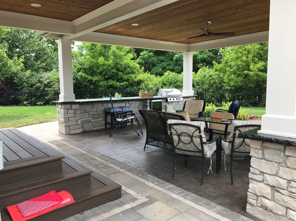 This is an example of a mid-sized traditional backyard patio in Chicago with an outdoor kitchen, concrete pavers and a roof extension.