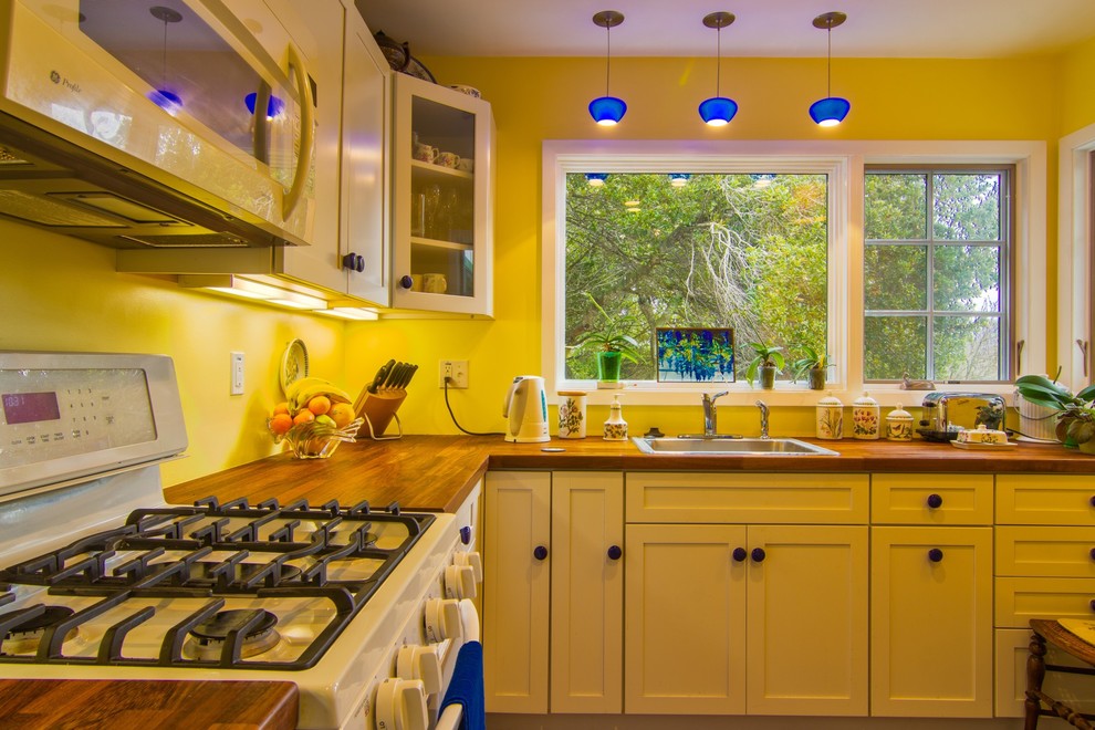 This is an example of a traditional kitchen in San Francisco with a drop-in sink, shaker cabinets, white cabinets, wood benchtops and white appliances.