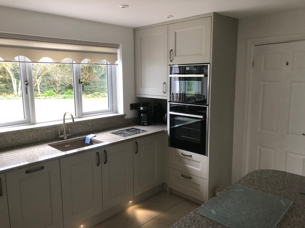 Small classic l-shaped kitchen/diner in Cardiff with a submerged sink, shaker cabinets, beige cabinets, quartz worktops, brown splashback, glass sheet splashback, black appliances, porcelain flooring, a breakfast bar, beige floors, multicoloured worktops and feature lighting.