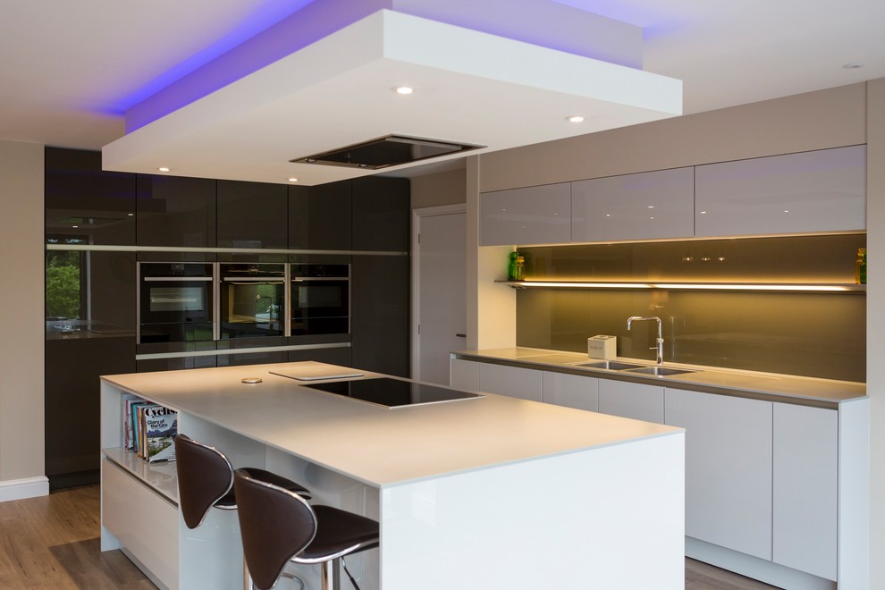 Design ideas for a large contemporary galley open plan kitchen in Other with a double-bowl sink, flat-panel cabinets, white cabinets, glass benchtops, grey splashback, glass sheet splashback, black appliances, light hardwood floors and with island.