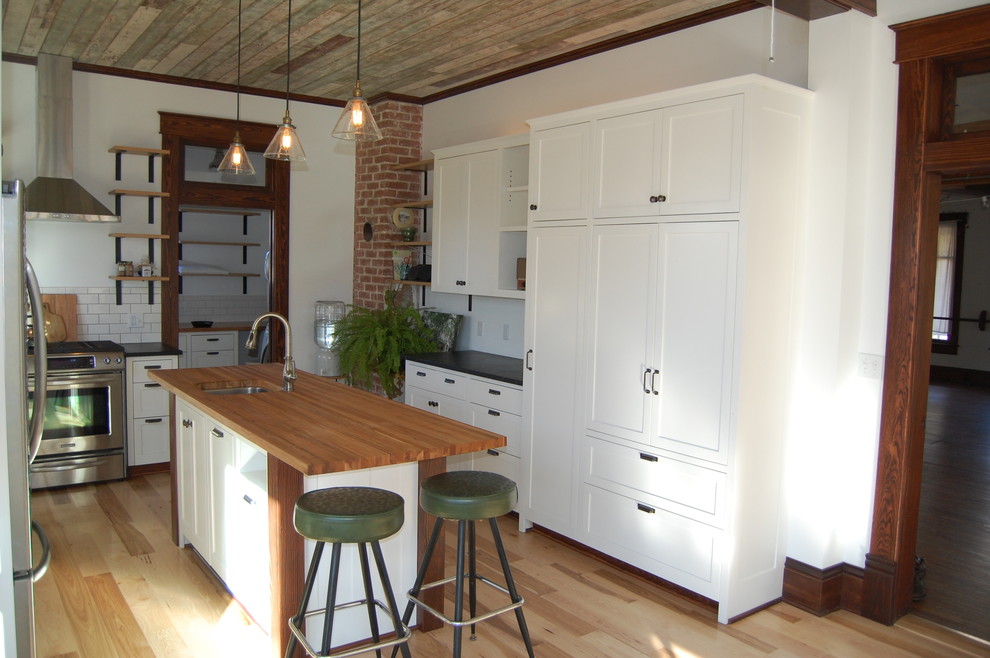 Mid-sized transitional l-shaped light wood floor enclosed kitchen photo with an undermount sink, shaker cabinets, white cabinets, soapstone countertops, white backsplash, subway tile backsplash and an island