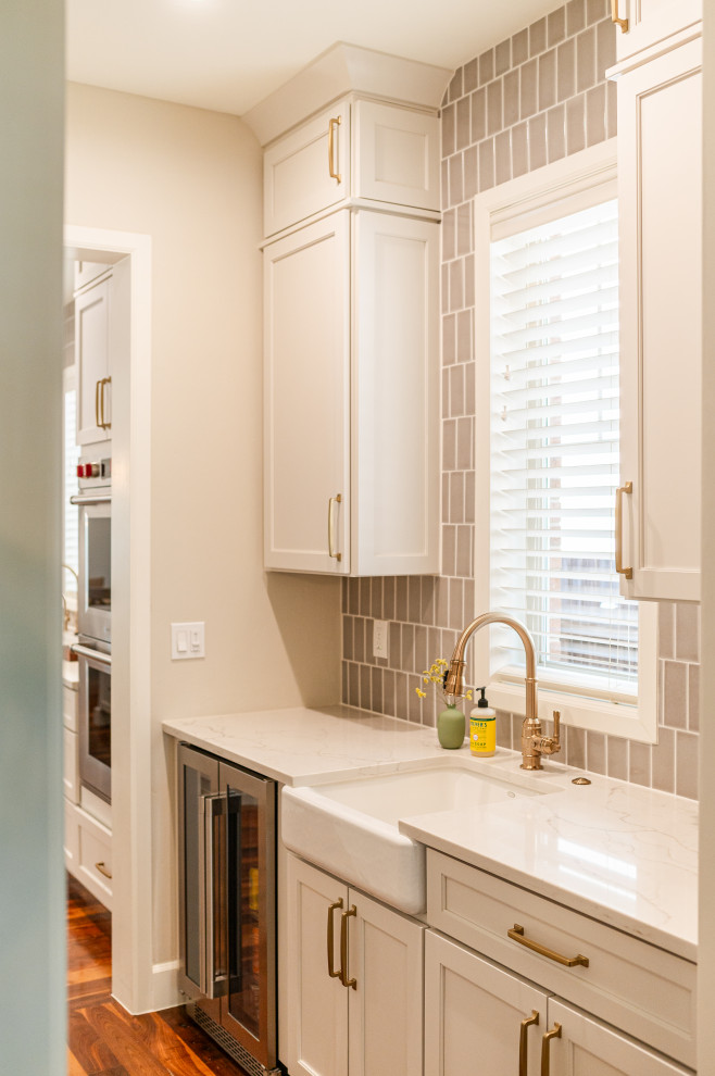 Large transitional l-shaped dark wood floor and brown floor open concept kitchen photo in Denver with a farmhouse sink, shaker cabinets, beige cabinets, quartz countertops, beige backsplash, ceramic backsplash, stainless steel appliances, an island and white countertops
