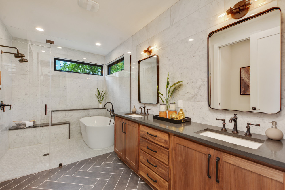 Photo of an ensuite bathroom in Austin with recessed-panel cabinets, brown cabinets, a freestanding bath, a built-in shower, white tiles, marble tiles, ceramic flooring, a submerged sink, grey floors, a hinged door, grey worktops, double sinks and a built in vanity unit.