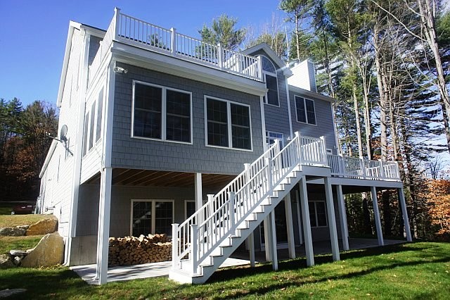 This is an example of a large contemporary two-storey grey house exterior in Manchester with vinyl siding, a gable roof and a shingle roof.