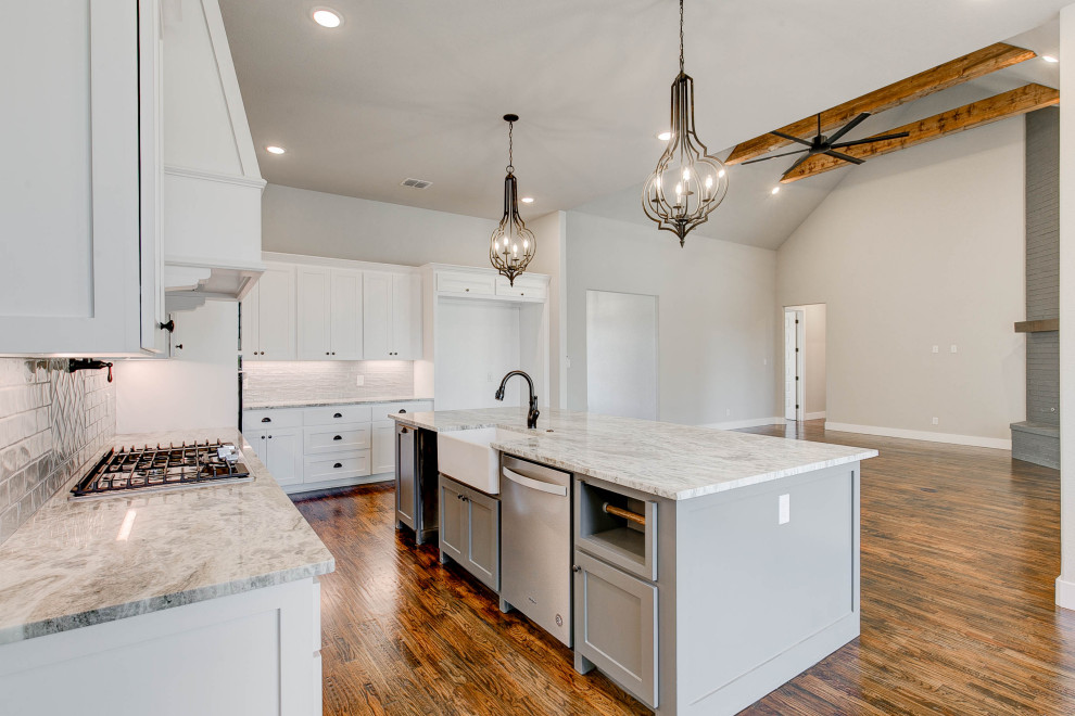 This is an example of a mid-sized single-wall open plan kitchen in Dallas with a farmhouse sink, flat-panel cabinets, white cabinets, quartzite benchtops, white splashback, subway tile splashback, stainless steel appliances, dark hardwood floors, with island, brown floor and white benchtop.