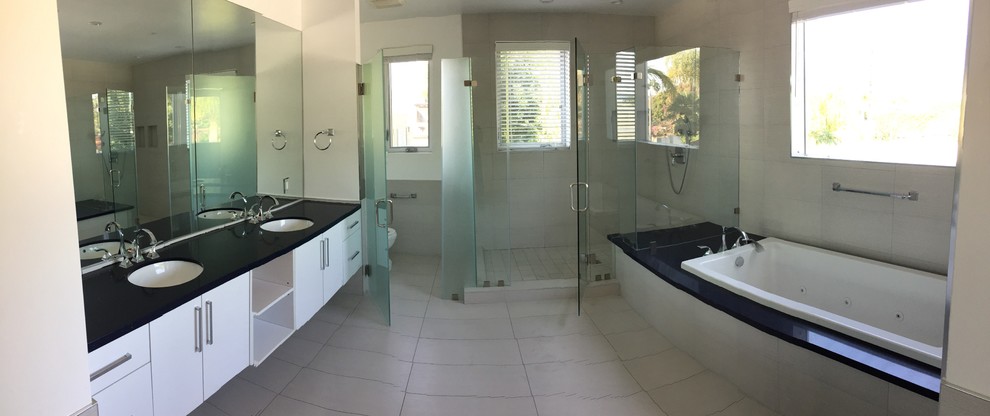 Large contemporary master bathroom in Los Angeles with flat-panel cabinets, white cabinets, a drop-in tub, a corner shower, a two-piece toilet, white walls, ceramic floors, an undermount sink, solid surface benchtops, grey floor, a hinged shower door, gray tile and cement tile.