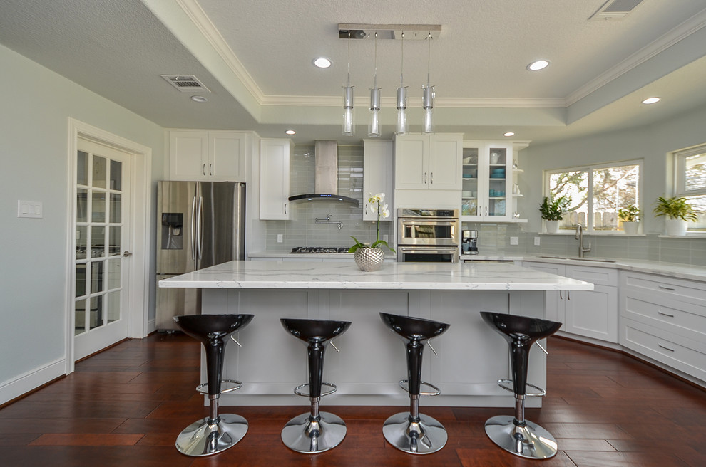 This is an example of a mid-sized modern kitchen in Houston with a single-bowl sink, shaker cabinets, white cabinets, quartz benchtops, grey splashback, glass tile splashback, stainless steel appliances, medium hardwood floors, with island and red floor.