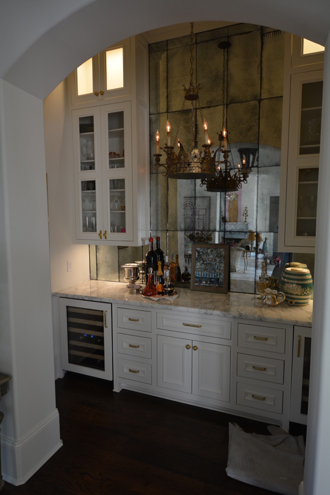 This is an example of a mid-sized traditional single-wall home bar in New Orleans with recessed-panel cabinets, white cabinets, marble benchtops, mirror splashback and dark hardwood floors.