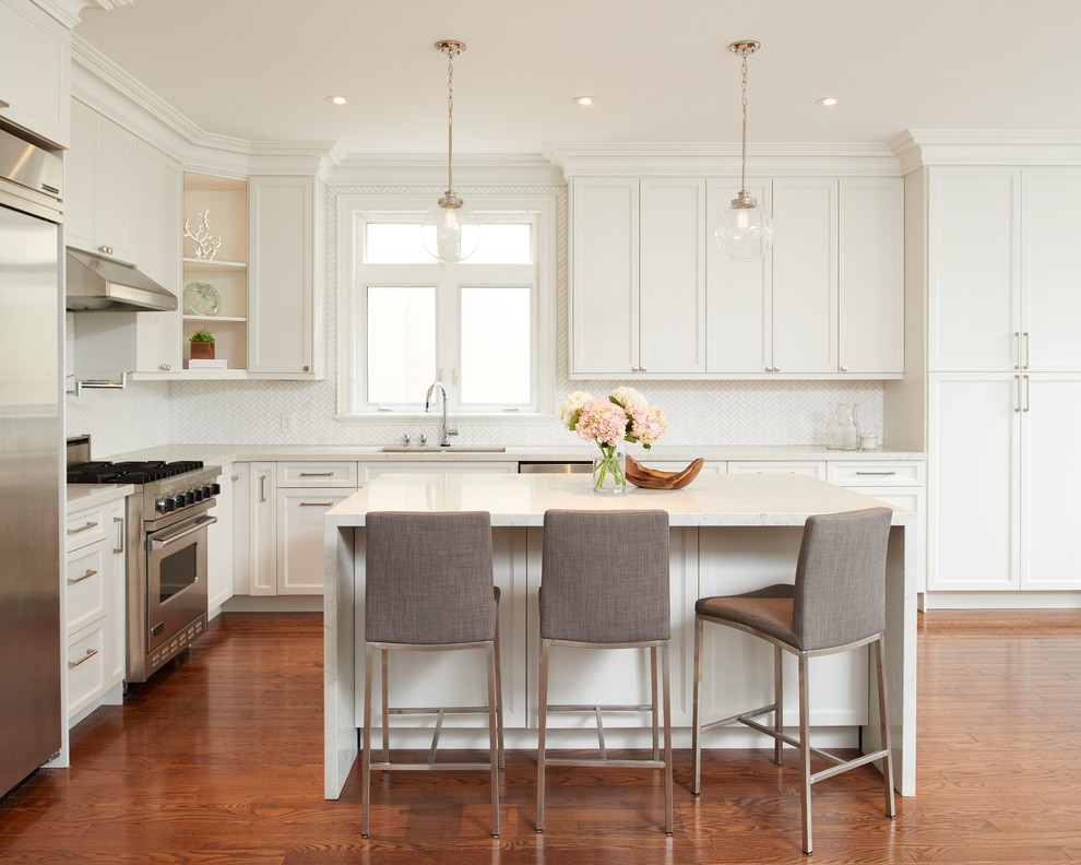 This is an example of a transitional l-shaped kitchen in Toronto with an undermount sink, recessed-panel cabinets, white cabinets, white splashback, stainless steel appliances, medium hardwood floors and with island.
