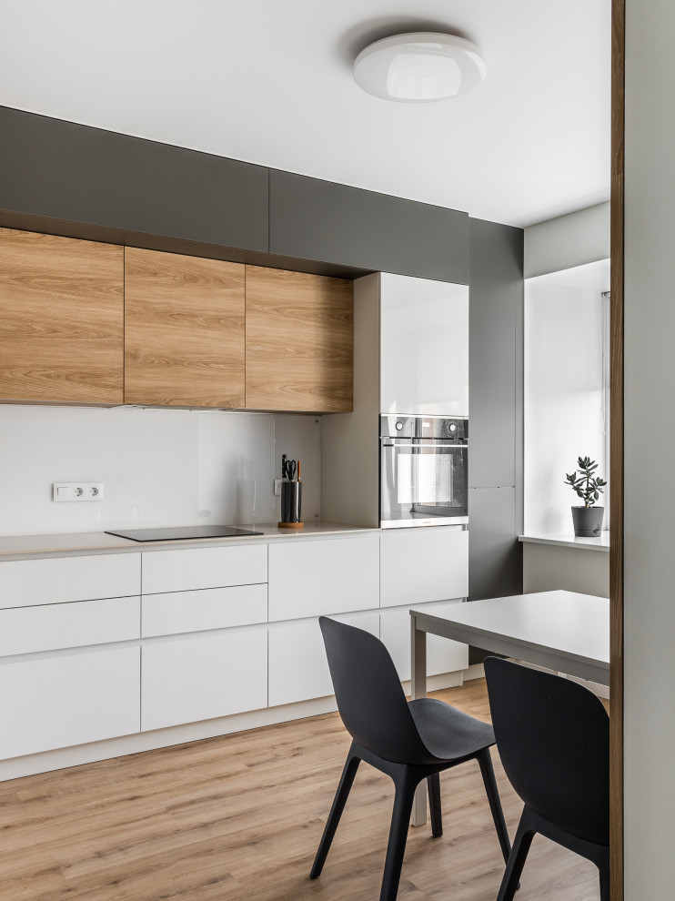 Mid-sized contemporary l-shaped eat-in kitchen in Other with a single-bowl sink, flat-panel cabinets, white cabinets, solid surface benchtops, white splashback, glass sheet splashback, black appliances, vinyl floors, no island, beige floor and beige benchtop.