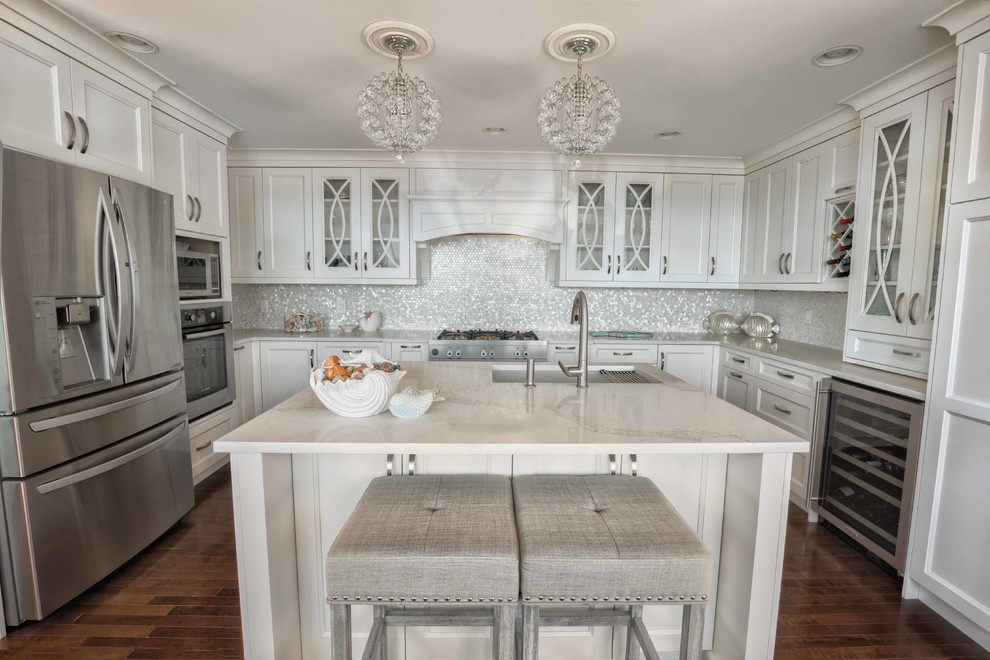 This is an example of a mid-sized transitional l-shaped eat-in kitchen in Vancouver with an undermount sink, raised-panel cabinets, white cabinets, marble benchtops, white splashback, mosaic tile splashback, stainless steel appliances, medium hardwood floors, with island and brown floor.