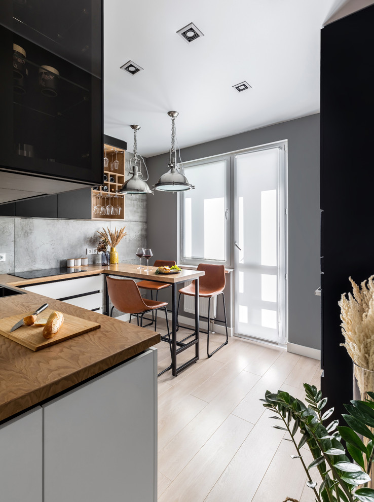 Small contemporary l-shaped eat-in kitchen in Saint Petersburg with an undermount sink, flat-panel cabinets, black cabinets, wood benchtops, grey splashback, porcelain splashback, black appliances, laminate floors, no island, beige floor and beige benchtop.