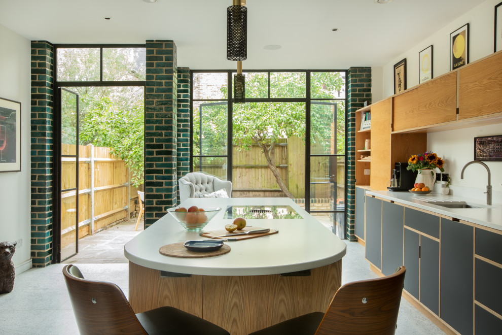 Photo of a large contemporary open plan kitchen in London with a drop-in sink, flat-panel cabinets, quartz benchtops, white splashback, engineered quartz splashback, terrazzo floors, with island, multi-coloured floor and white benchtop.