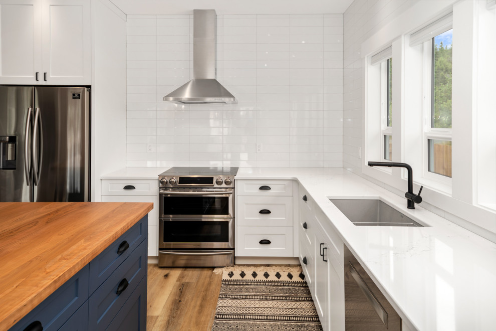 Inspiration for a mid-sized country l-shaped eat-in kitchen in Vancouver with a drop-in sink, shaker cabinets, yellow cabinets, quartz benchtops, white splashback, subway tile splashback, stainless steel appliances, laminate floors, with island, brown floor and white benchtop.