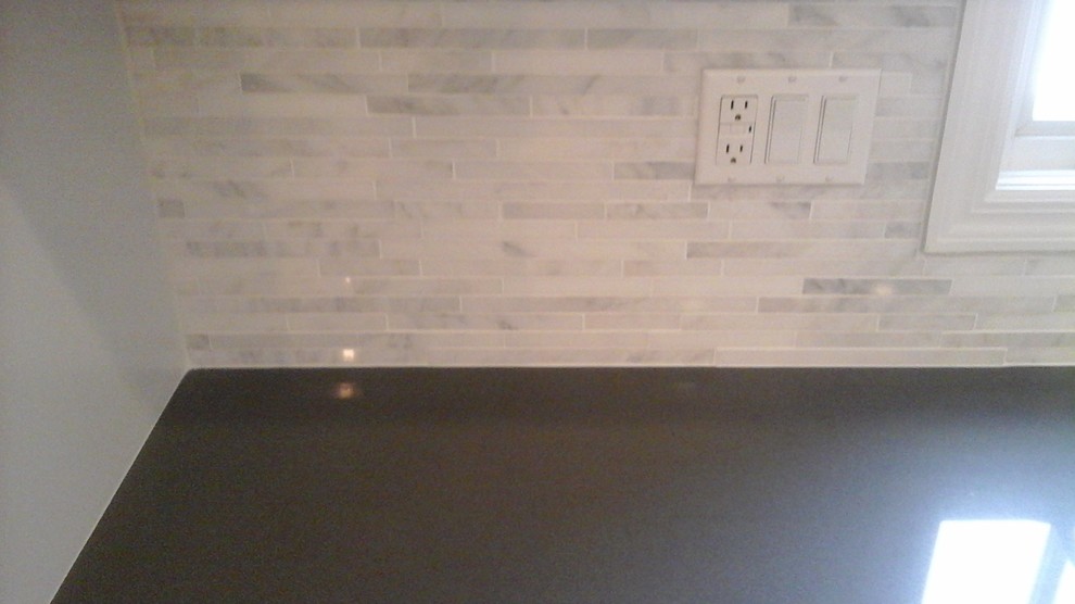 Inspiration for a mid-sized transitional l-shaped light wood floor eat-in kitchen remodel in Newark with a double-bowl sink, shaker cabinets, white cabinets, solid surface countertops, multicolored backsplash, stone tile backsplash, stainless steel appliances and an island