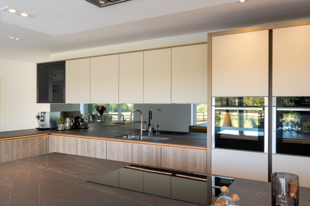 This is an example of a large contemporary l-shaped open plan kitchen in Hampshire with flat-panel cabinets, white cabinets, grey splashback, glass sheet splashback, porcelain floors, with island, multi-coloured floor and grey benchtop.