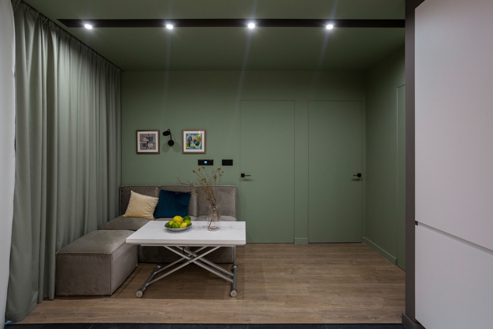 Modelo de salón actual de tamaño medio sin chimenea con paredes verdes, suelo laminado y suelo marrón