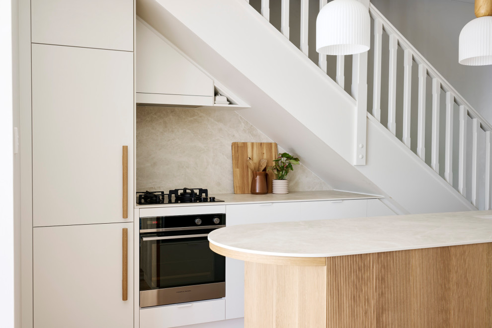 This is an example of a small scandinavian galley eat-in kitchen in Perth with an undermount sink, flat-panel cabinets, white cabinets, quartz benchtops, beige splashback, porcelain splashback, black appliances, light hardwood floors, with island, brown floor, beige benchtop and vaulted.