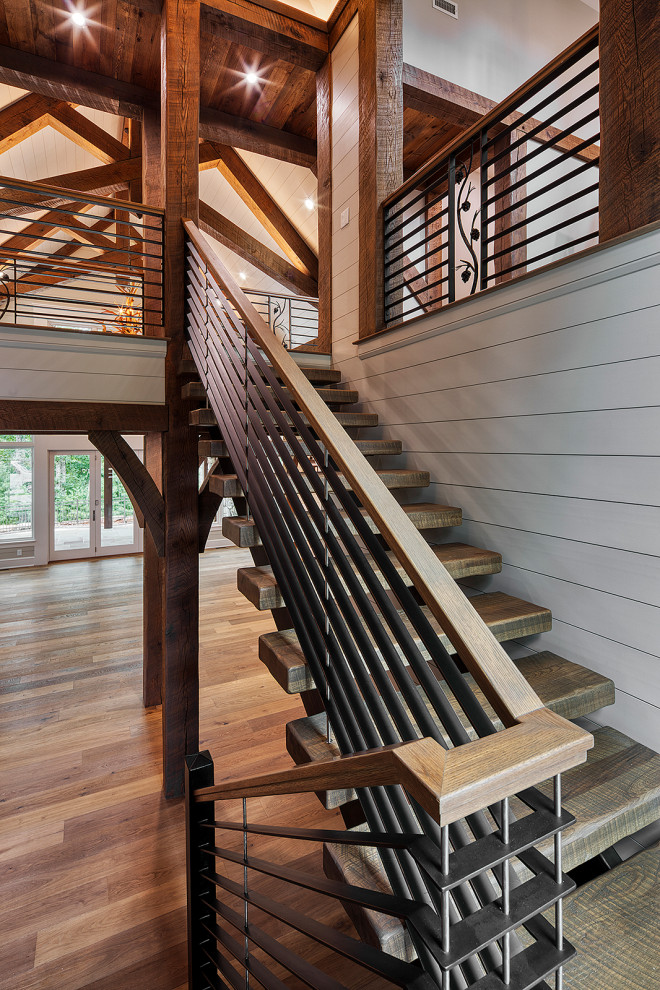 На фото: лестница на больцах, среднего размера в стиле кантри с деревянными ступенями, металлическими перилами и стенами из вагонки без подступенок