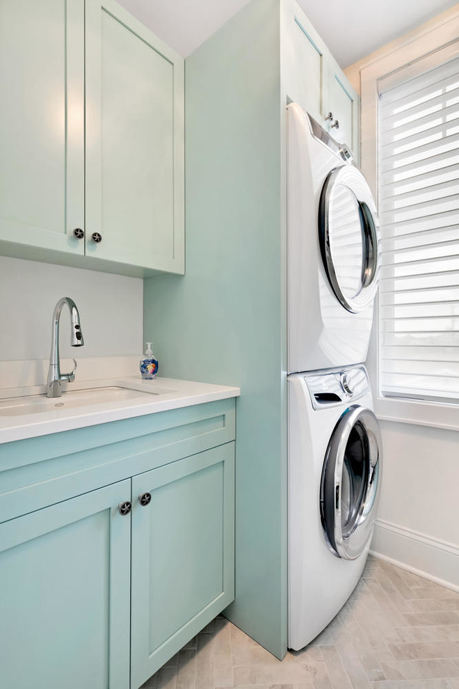 Design ideas for a beach style dedicated laundry room in New York with an undermount sink, shaker cabinets, blue cabinets, quartz benchtops, white walls, ceramic floors, a stacked washer and dryer, white floor and white benchtop.