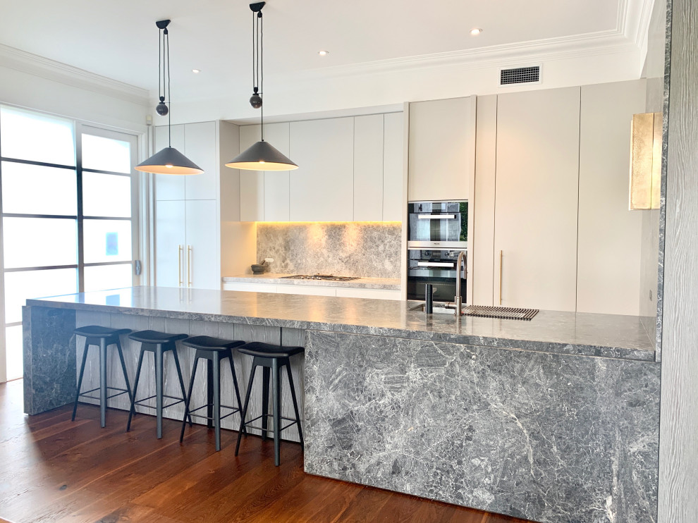 Inspiration for a large contemporary galley kitchen in Melbourne with grey cabinets, grey splashback, stone slab splashback, black appliances, dark hardwood floors, with island, brown floor, grey benchtop, an undermount sink and flat-panel cabinets.