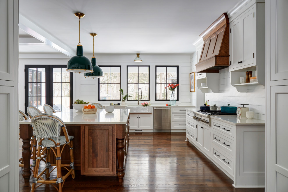 Inspiration for a large country u-shaped open plan kitchen in Chicago with a farmhouse sink, recessed-panel cabinets, white cabinets, quartz benchtops, white splashback, shiplap splashback, stainless steel appliances, medium hardwood floors, with island, brown floor and white benchtop.