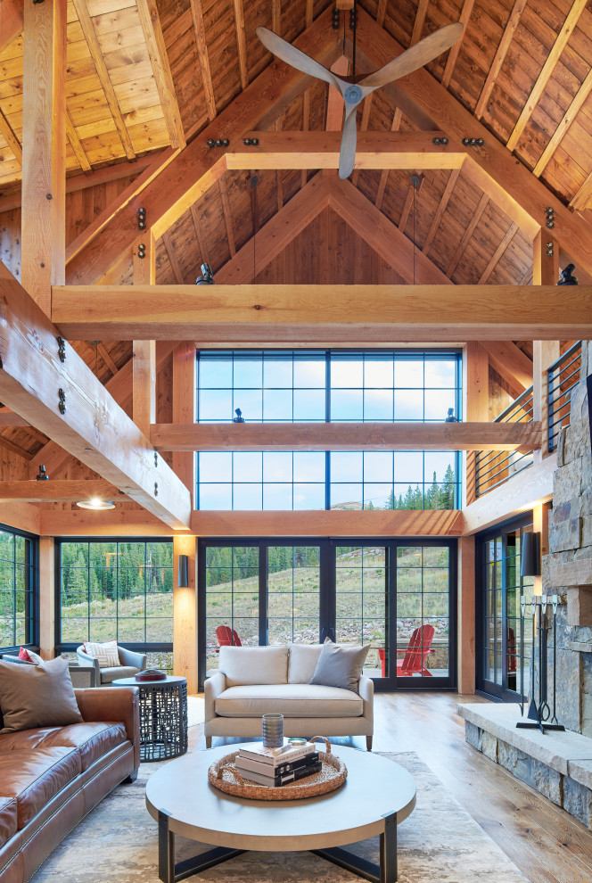 Large mountain style open concept medium tone wood floor, brown floor, exposed beam, vaulted ceiling and wood ceiling living room photo in Other with brown walls, a standard fireplace and a stone fireplace