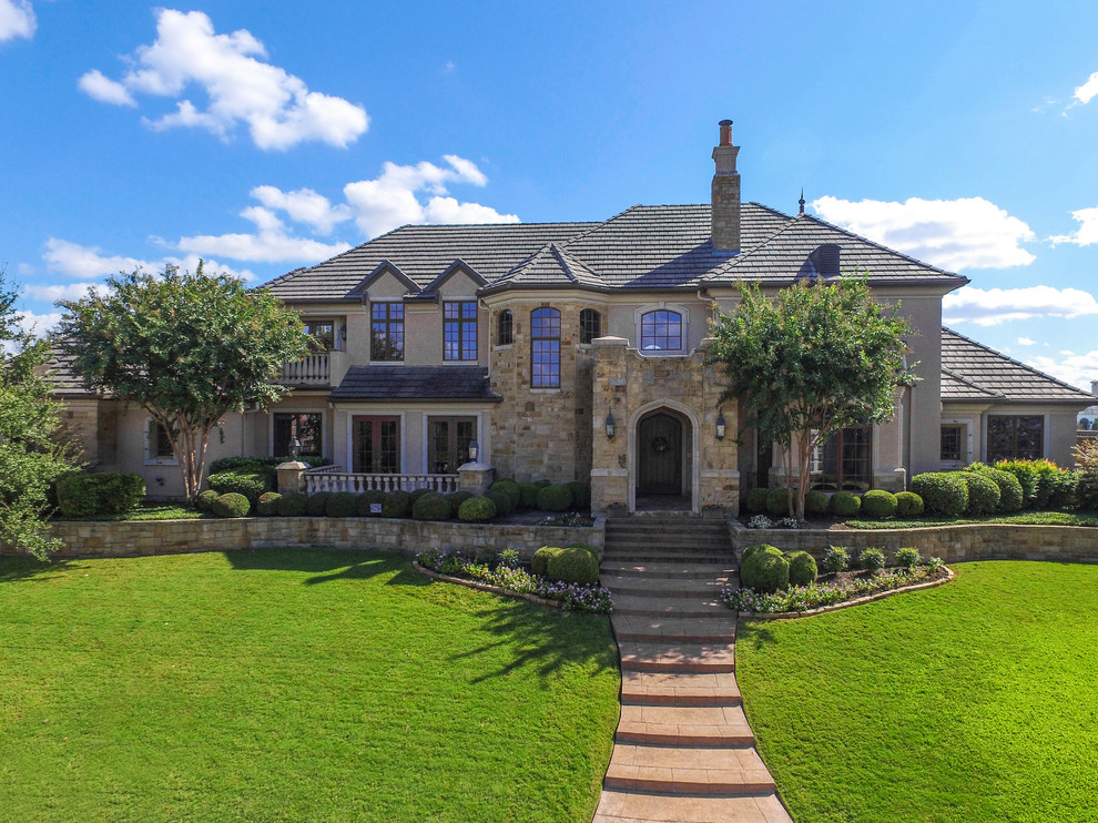 Large traditional two-storey beige house exterior in Dallas with stone veneer, a gambrel roof and a shingle roof.