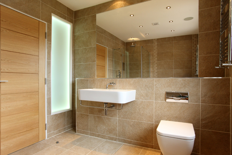 Design ideas for a mid-sized modern master wet room bathroom in London with a drop-in tub, a wall-mount toilet, beige tile, ceramic tile, beige walls, a wall-mount sink, tile benchtops, an open shower and beige benchtops.
