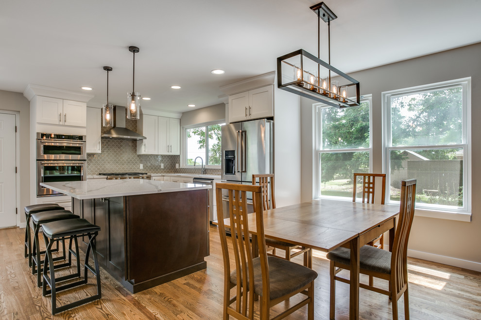 Photo of a large transitional l-shaped open plan kitchen in Seattle with an undermount sink, shaker cabinets, white cabinets, quartzite benchtops, beige splashback, ceramic splashback, stainless steel appliances, medium hardwood floors, with island and brown floor.