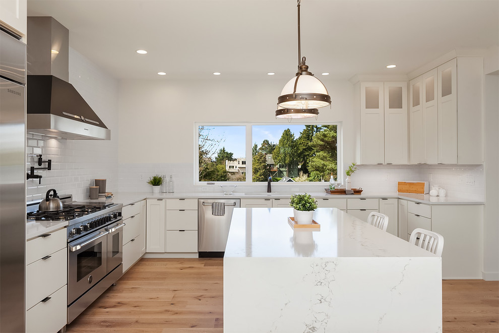 Contemporary l-shaped kitchen in Seattle with an undermount sink, shaker cabinets, white cabinets, white splashback, subway tile splashback, stainless steel appliances, medium hardwood floors, with island and brown floor.