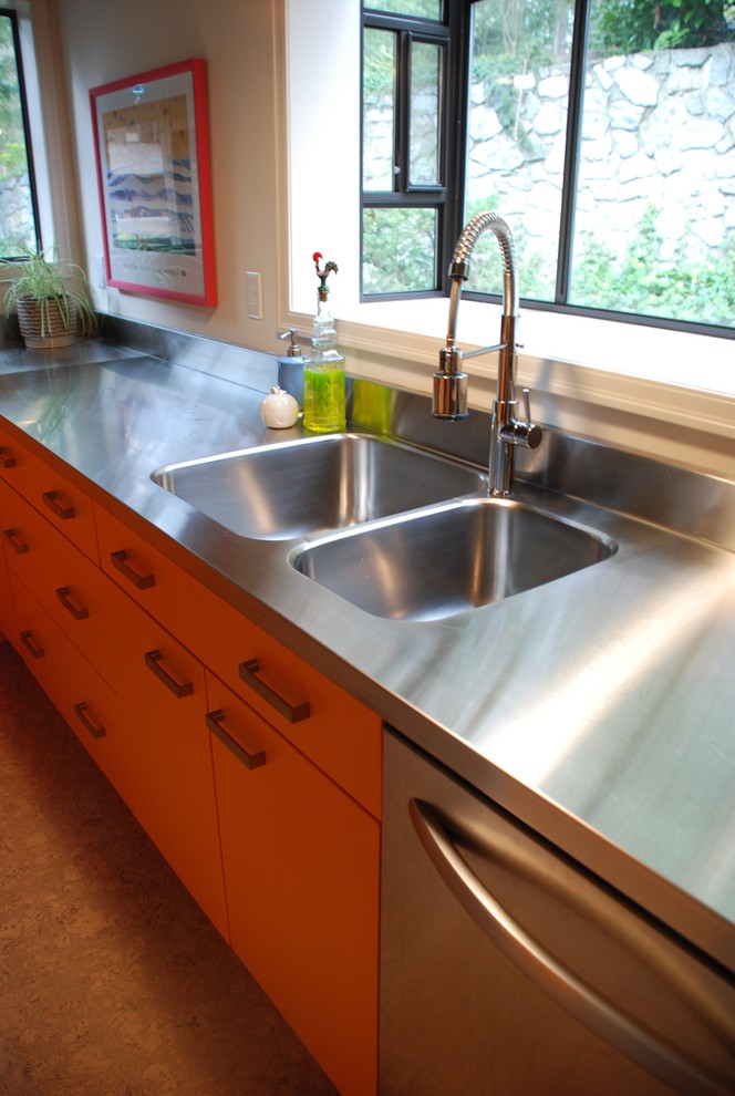This is an example of a midcentury kitchen in Vancouver with an integrated sink, flat-panel cabinets, orange cabinets, stainless steel benchtops, metallic splashback, metal splashback and stainless steel appliances.