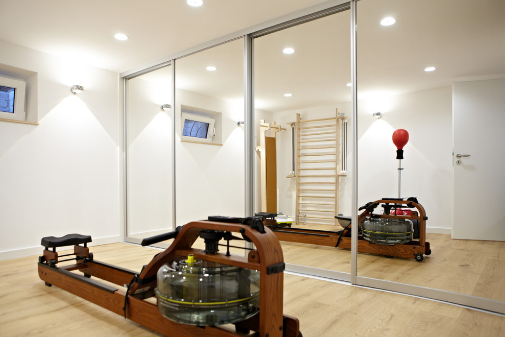 Inspiration for a mid-sized modern home weight room in Dusseldorf with white walls and light hardwood floors.