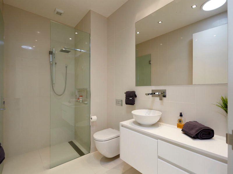 Photo of a mid-sized contemporary bathroom in Melbourne with a vessel sink, flat-panel cabinets, engineered quartz benchtops, an open shower, a wall-mount toilet, white tile, porcelain tile, white walls, porcelain floors and white cabinets.