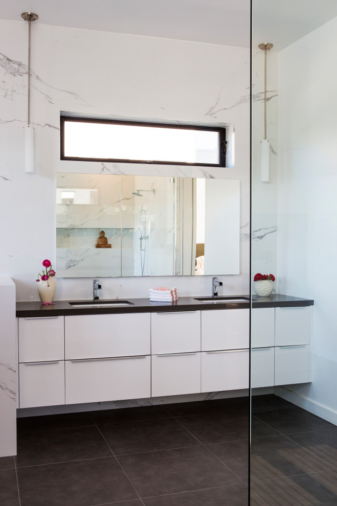 Photo of a large modern ensuite bathroom in Los Angeles with flat-panel cabinets, white cabinets, a freestanding bath, a corner shower, white tiles, porcelain tiles, white walls, porcelain flooring, a submerged sink, solid surface worktops, grey floors, an open shower, grey worktops, a shower bench, double sinks and a built in vanity unit.