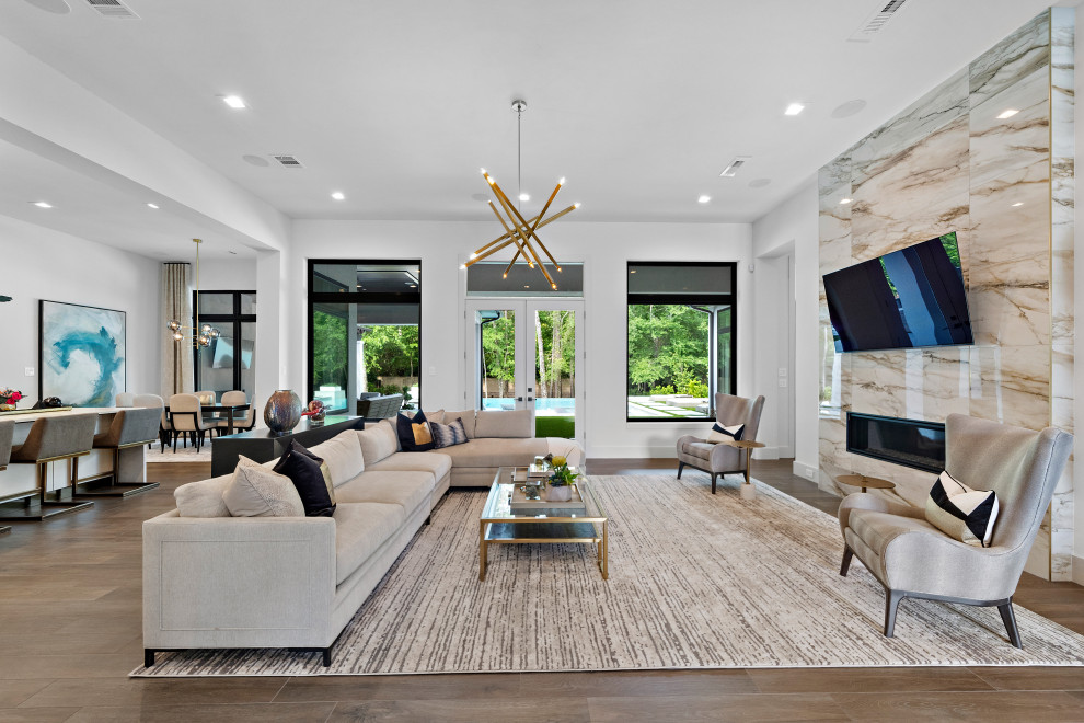 Large modern open concept living room in Houston with white walls, porcelain floors, a standard fireplace, a tile fireplace surround, a wall-mounted tv and brown floor.