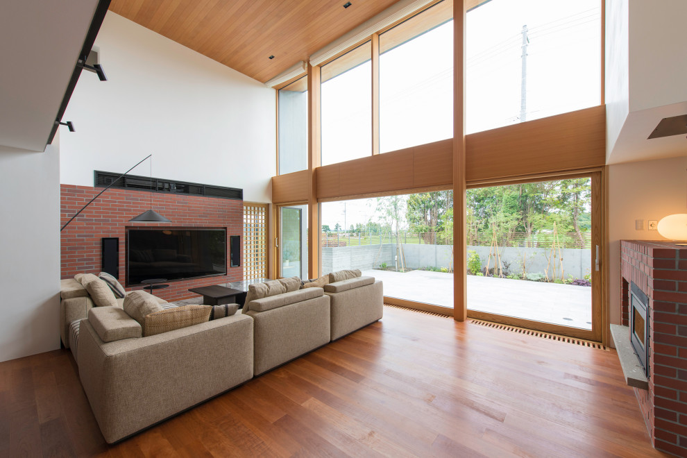 Large modern formal open concept living room with white walls, plywood floors, a standard fireplace, a brick fireplace surround, a wall-mounted tv and brown floor.