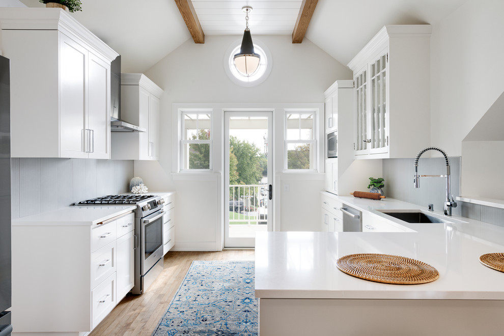 Design ideas for a mid-sized transitional u-shaped eat-in kitchen in Minneapolis with white cabinets, stainless steel appliances, a peninsula, brown floor, an undermount sink, shaker cabinets, grey splashback, medium hardwood floors and white benchtop.