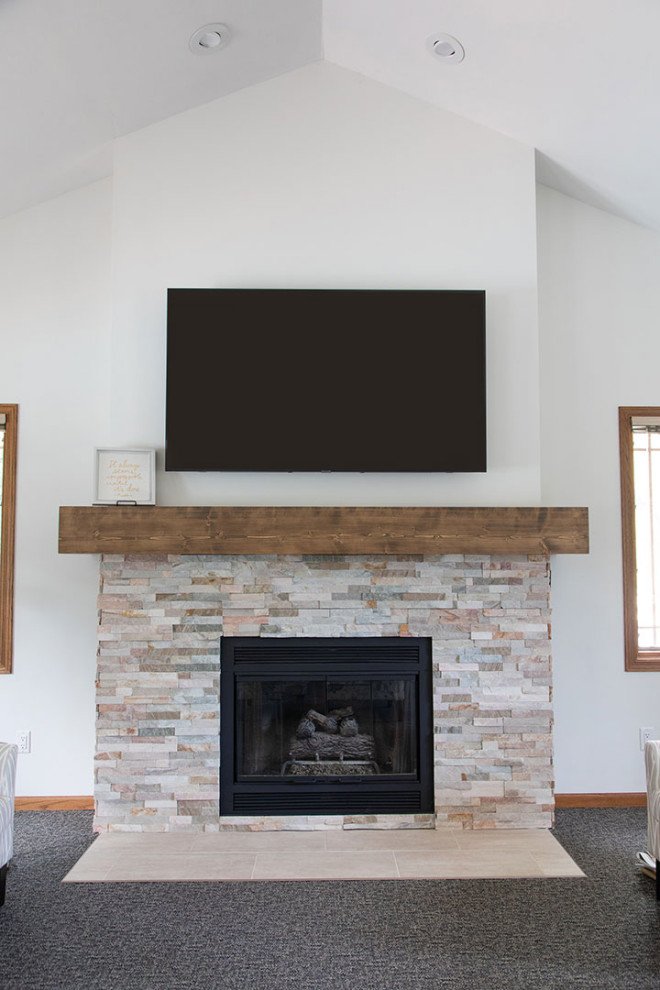 他の地域にある広いトランジショナルスタイルのおしゃれなLDK (カーペット敷き、標準型暖炉、積石の暖炉まわり、壁掛け型テレビ、グレーの床、塗装板張りの天井) の写真
