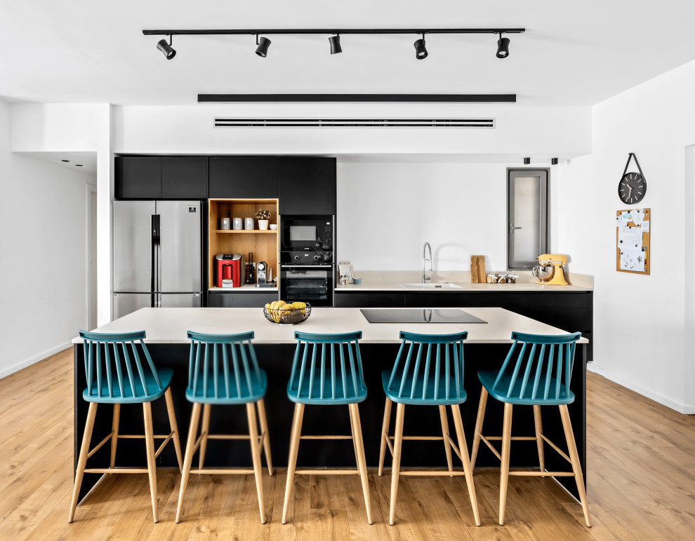 Zweizeilige Moderne Küche mit flächenbündigen Schrankfronten, schwarzen Schränken, braunem Holzboden, Kücheninsel, braunem Boden und beiger Arbeitsplatte in Tel Aviv