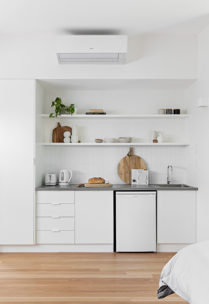 Small contemporary single-wall wet bar in Sydney with a drop-in sink, flat-panel cabinets, white cabinets, white splashback, light hardwood floors, beige floor and grey benchtop.