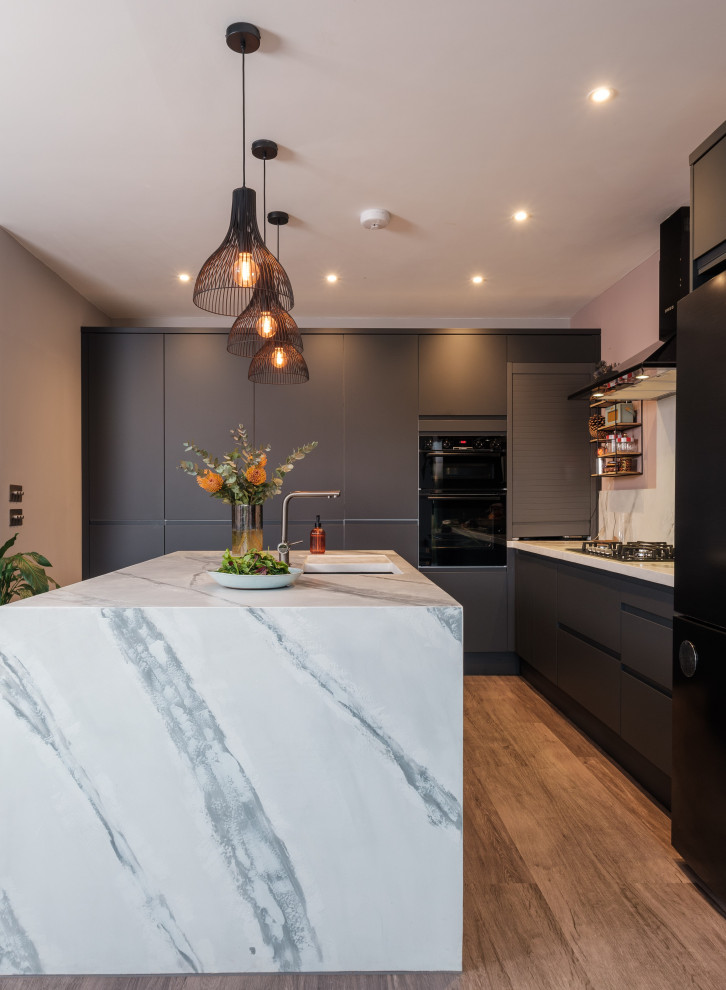 This is an example of a large modern kitchen in London with a submerged sink, flat-panel cabinets, blue cabinets, white splashback, black appliances, an island and brown floors.